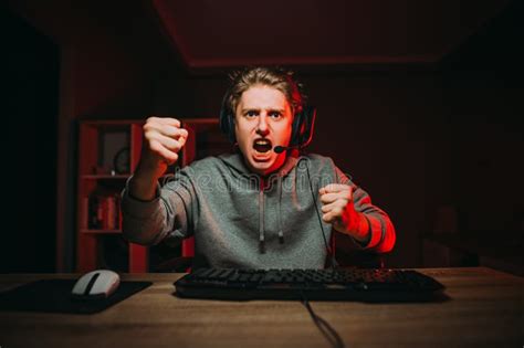 Angry Young Male Gamer In Headset Looks At Screen And Shows Fist During