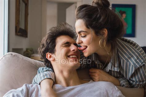 Cheerful Woman Licking Nose Of Smiling Man On Couch At Home — Love