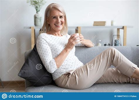 Portrait Of Smiling Mature Woman Relaxing On Couch With Cup Stock Photo