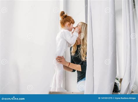 happy mother kissing little redhead daughter near large window with the white curtains stock