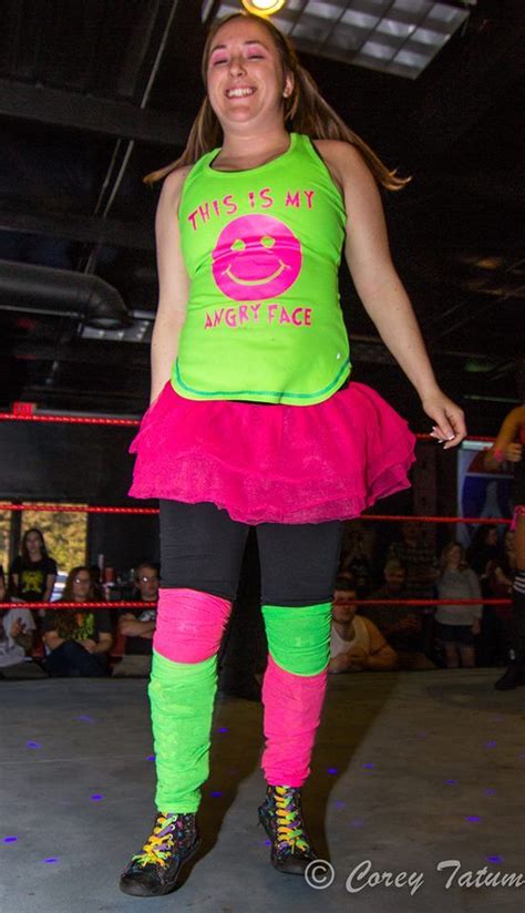 A Woman In A Green Shirt And Pink Skirt Standing On Top Of A Wrestling Ring