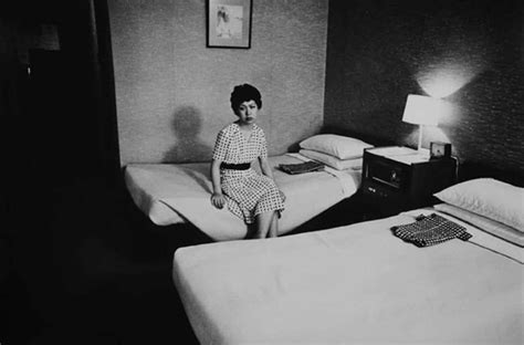 A Black And White Photo Of A Woman Sitting On Two Beds In A Hotel Room