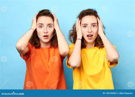 Emotional Women With Wide Open Eyes Holding Heads On Blue Background