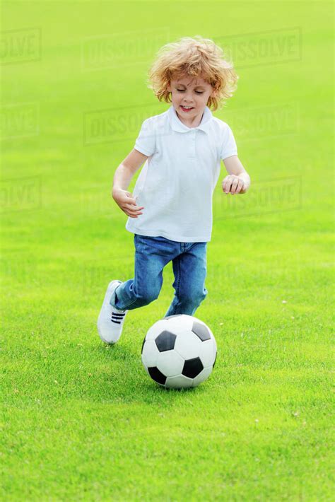 Cute Happy Little Boy Playing Soccer On Green Grass At Park Stock