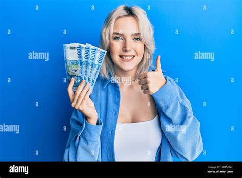 Young Blonde Girl Holding Hungarian Forint Banknotes Smiling Happy And Positive Thumb Up Doing