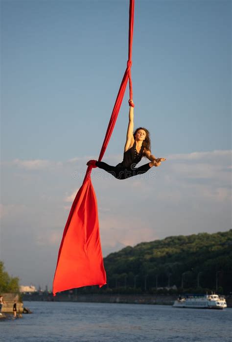 beautiful and flexible female circus artist dancing with aerial silk with sky and river