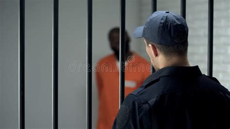 Jail Warden With Keys Looking At African American Imprisoned Criminal