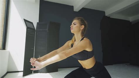 Side View Portrait Of A Young Blonde Woman Doing Squats While Standing