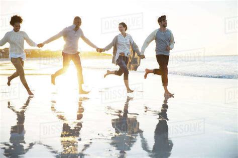 Group Of Four Friends Holding Hands And Running On Beach Stock Photo Dissolve
