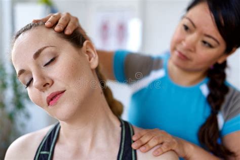 Chinese Woman Massage Therapist Giving A Neck And Back Pressure Treatment To An Attractive Blond