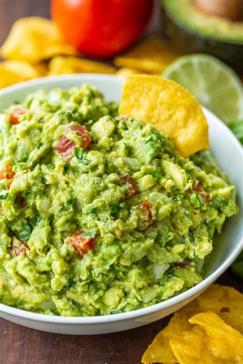 A White Bowl Filled With Guacamole Surrounded By Tortilla Chips And