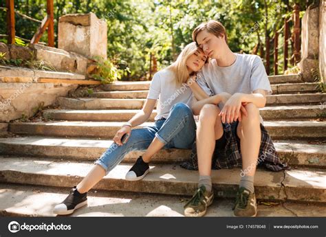 Young Beautiful Couple Sitting On Stairs In Park And Dreamily Closing