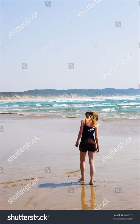 Blonde Woman Walking On The Beach Picking Up Shells Movement On Hair That Is Blowing In The