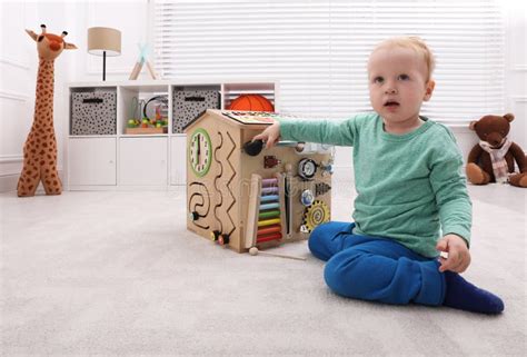 Cute Little Boy Playing With Busy Board House On Floor Stock Photo