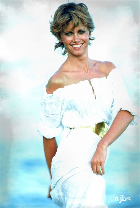 A Woman In A White Dress Standing On The Beach With Her Arms Behind Her