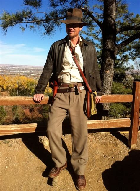 A Man Wearing A Hat And Tie Standing In Front Of A Wooden Fence With