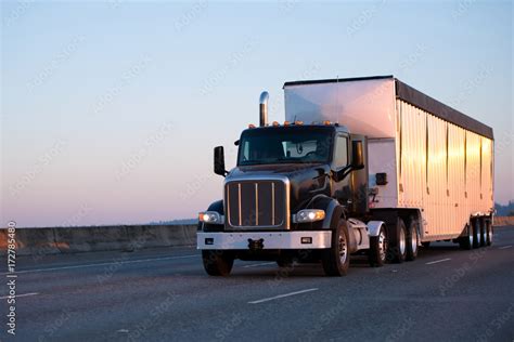 Dark Big Rig Semi Truck With Bulk Trailer Running On Highway In Sunset
