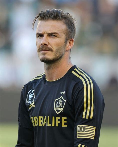 A Man With A Goatee Standing In Front Of A Soccer Field Wearing A Black