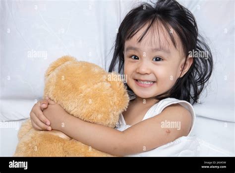 Asian Little Chinese Girl Hugging A Teddy Bear On The Bed At Home Stock