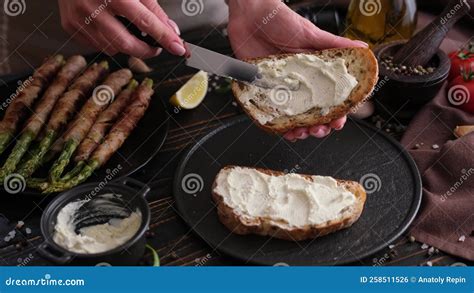 Spreading Cream Cheese On Slice Of Bread At Domestic Kitchen Stock