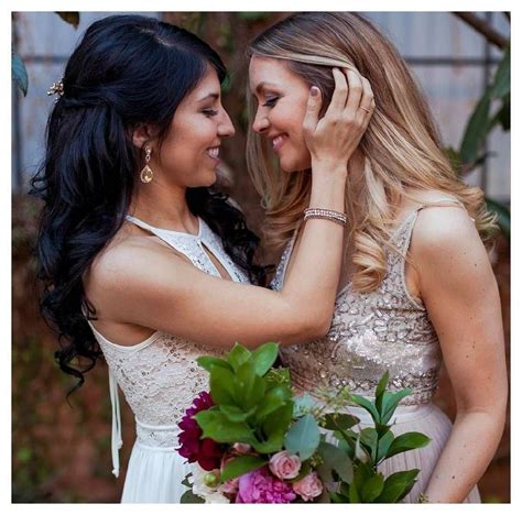 Two Beautiful Women Standing Next To Each Other In Front Of Flowers And Greenery