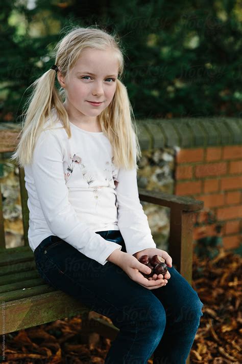 A Little Girl Sitting Outdoors With Her Hands Full Of Conkers By