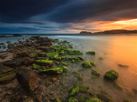 Sunset In Spain Coast Rocks With Green Moss Sea Reflection On Red Sky