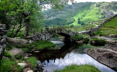 A Small Stream Running Through A Lush Green Hillside Covered In Grass