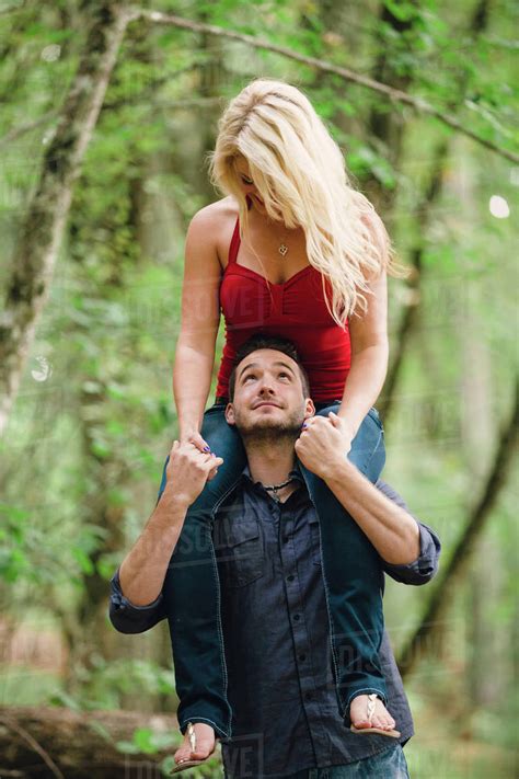 Portrait Of Young Man Standing In Forest And Carrying Blonde Woman On