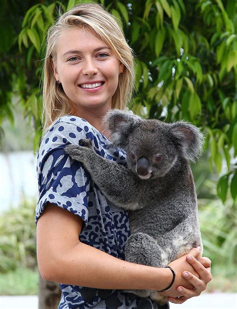 A Woman Holding A Koala In Her Arms And Smiling At The Camera With
