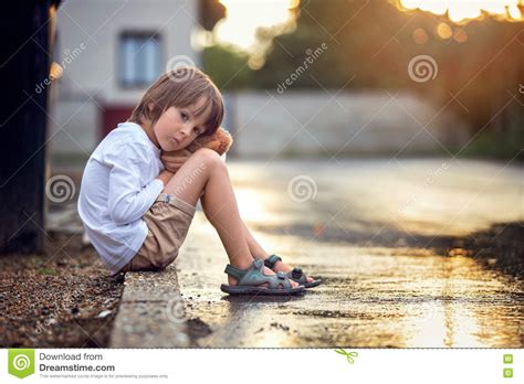 Sad Little Boy Sitting On The Street In The Rain Hugging