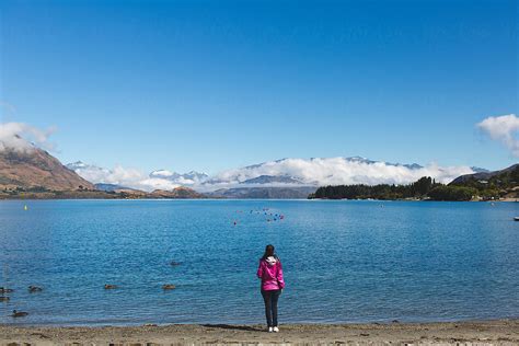 Woman Contemplating The Clouds Between The Mountains From A Lake Shore