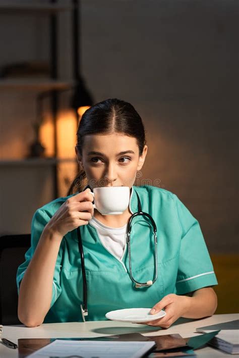 nurse in uniform sitting at table and drinking coffee during night shift stock image image of