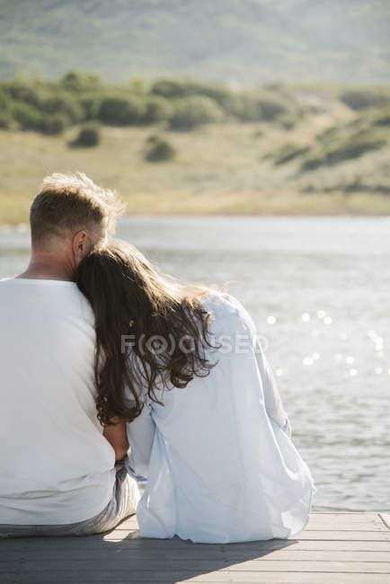 Woman Leaning On Male Shoulder While Sitting Side By Side On Jetty