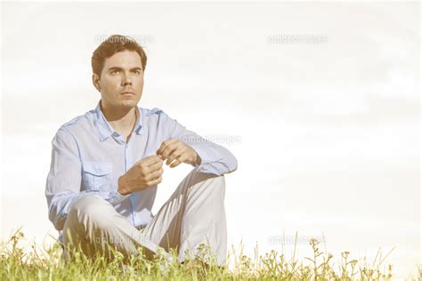 Thoughtful Young Man Looking Away While Sitting On Grass Against Clear