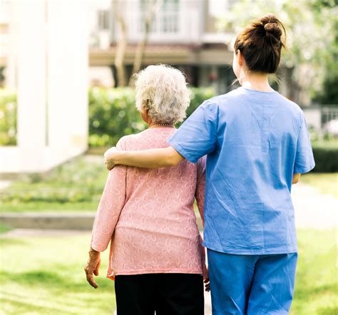 Back View Of Nurse Caregiver Support Walking With Elderly Woman Outdoor