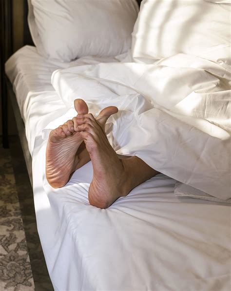 Feet Of A Sleeping Person Sticking Out From Under A Warm And Comfortable Blanket On The Bed