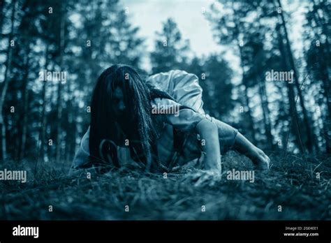 Girl With Long Black Hair In Image Of Scary Ghost Zombie Crawls On Ground In Dark Forest