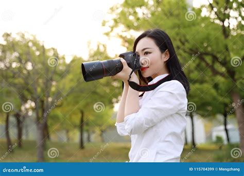 aisan chinese woman photographer hold camera close to her face work in nature against blue sky