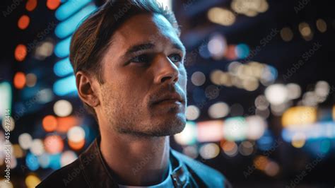 portrait of handsome serious man standing looking around night city with bokeh neon street