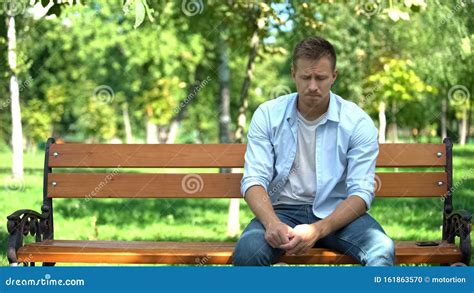 Man Alone In A Park Sitting On A Bench Under A Tree Stock Photo