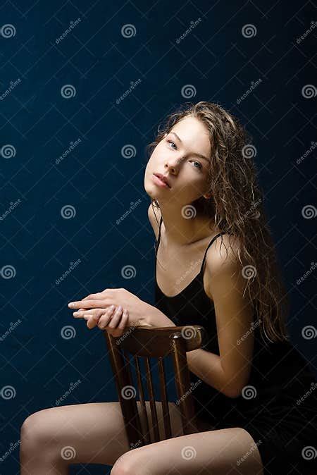 a girl with beautiful bright skin sits on a wooden chair wet curly hair lies on her shoulders