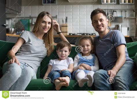 Portrait Of Happy Parents With Cute Kids Sitting On Sofa Stock Photo