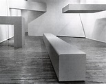 a black and white photo of a bench in a room with wooden floors ...