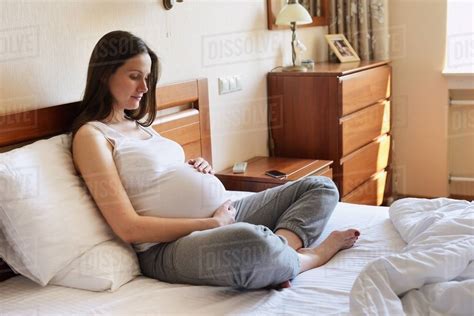 Pregnant Woman Sitting On Bed Holding Stomach Stock Photo Dissolve
