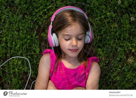 Portrait Of Girl Lying On A Meadow Listening Music With Pink Headphones