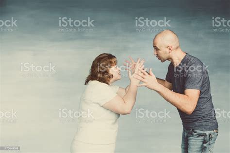 A Tall Bald Man And Plump Redhaired Attractive Woman On A Gray Background The Husband Scolds His