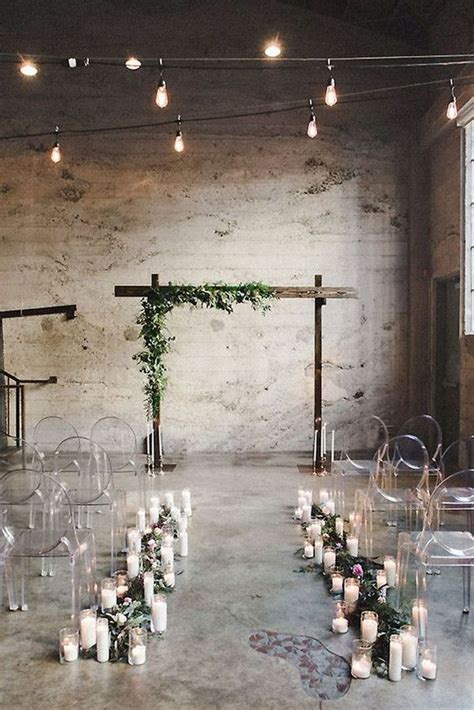 An Indoor Wedding Setup With Clear Chairs Candles And Greenery On The