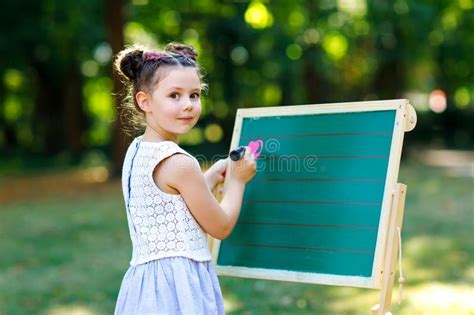 Happy Little Kid Girl Standing By Big Chalk Desk Preschool Or Schoolkid
