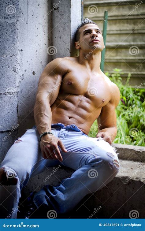 Muscular Young Latino Man Shirtless In Jeans Sitting Against Concrete